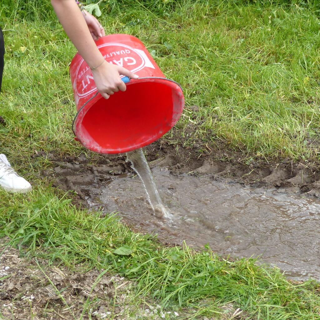 Ein Erdloch wird mit einem Kübel Wasser befüllt
