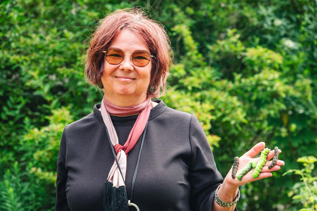Marion Jaros, Biotechnologin und Schmettelringszüchterin, lächelt mit Raupen auf der Hand in die Kamera 