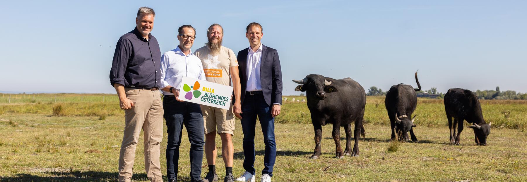 Vier Menschen stehen mit drei Wasserbüffeln im Hintergrund auf einer grünen Wiese
