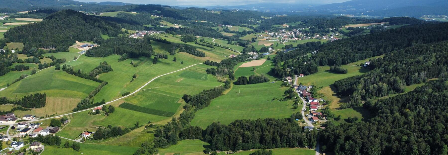 Luftbild das eine Mischung aus Wiesen, Waldstücken und Häusern entlang kleinerer Straßen