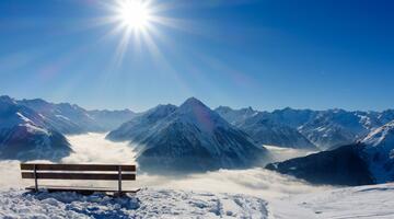 Bank in den schneebedeckten Bergen mit Ausblick auf Sonne und Gipfel