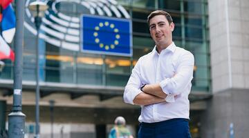 Mann steht vor Glashaus mit EU Flagge