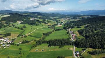 Luftbild das eine Mischung aus Wiesen, Waldstücken und Häusern entlang kleinerer Straßen